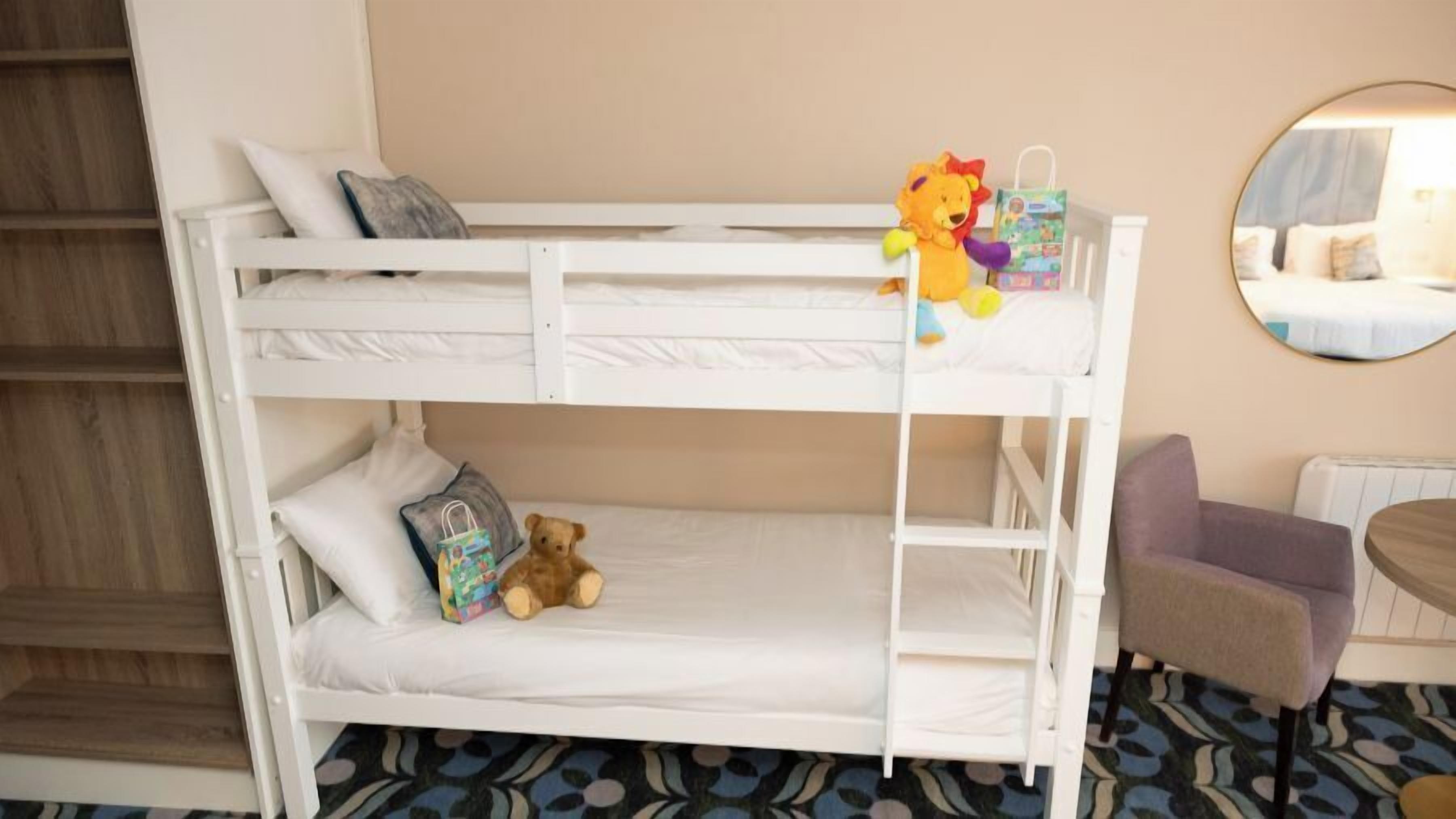 A bunk bed with a teddy bear and a gift bag on the top bunk.