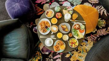 Una mesa redonda de comedor con diversos alimentos para el desayuno, como cruasanes, frutas y bebidas.