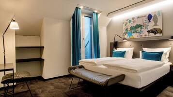 A modern hotel room with a bed, bench, desk, and a painting on the wall.