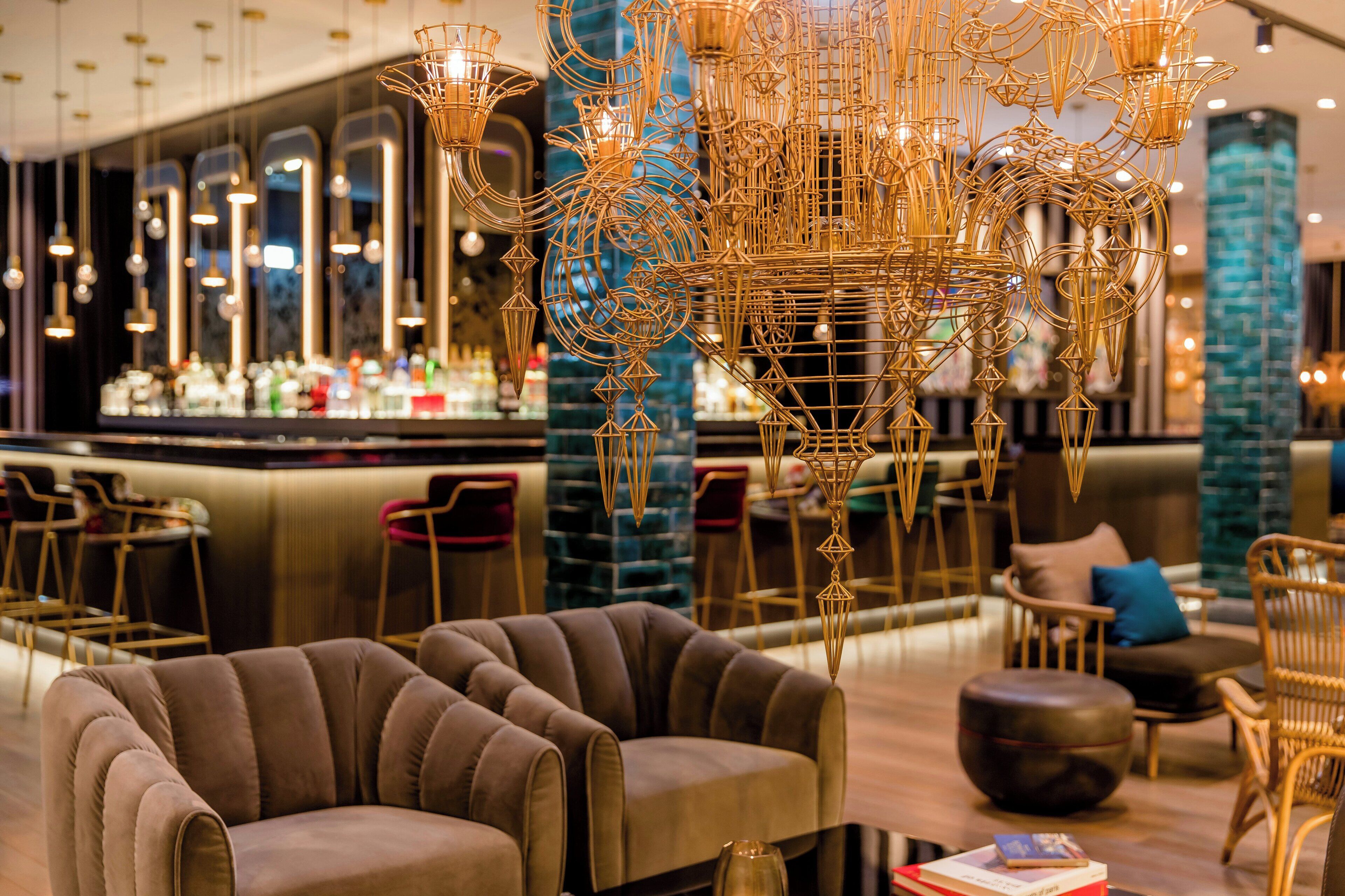 A modern bar area with a bar counter, seating with cushioned chairs, and a decorative chandelier.