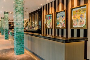 Una zona de bar con mostrador, pilares de azulejos verdes y obras de arte enmarcadas en la pared.