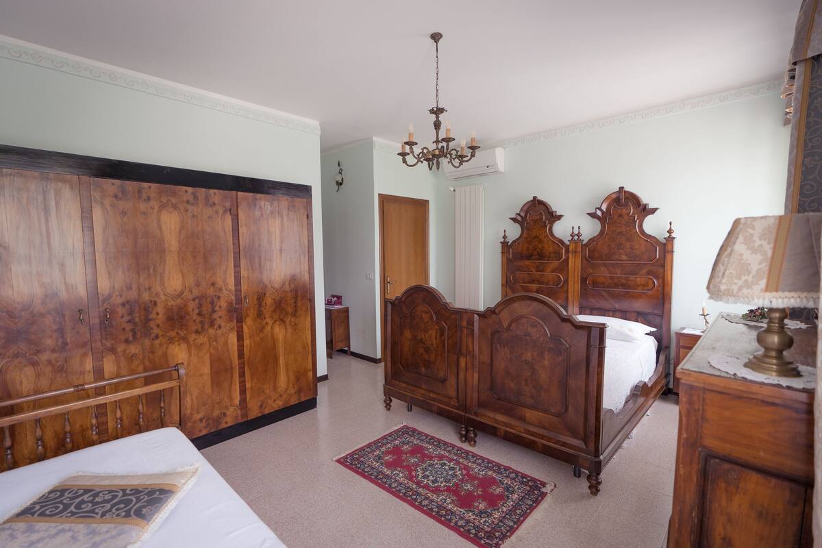 A bedroom with a large wardrobe, a wooden bed with a headboard, a chandelier, and a red rug.
