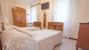 Un dormitorio con dos camas individuales, un armario de madera, un televisor montado en la pared y una silla.