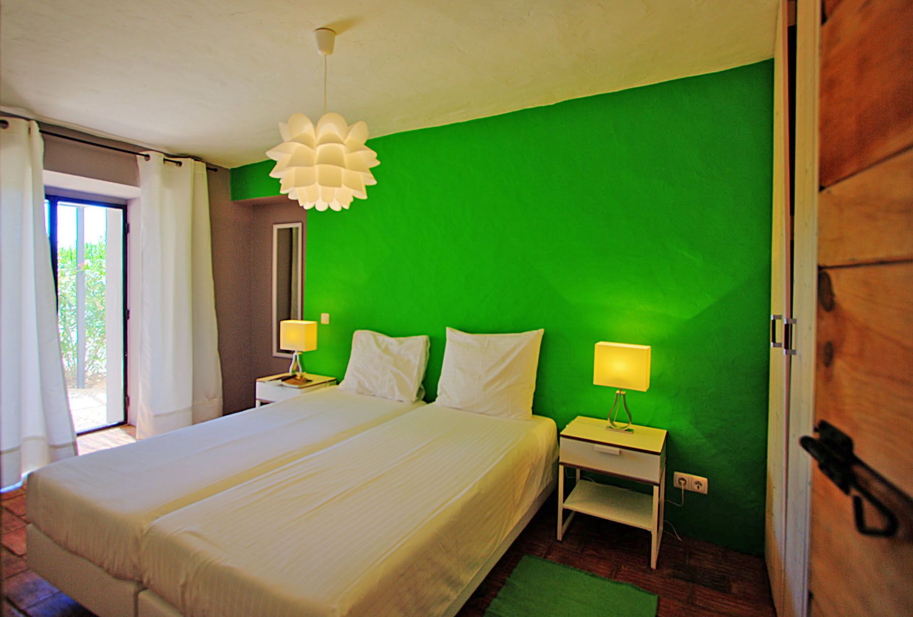 A hotel room with a large bed, two bedside tables with lamps, a green wall, and a wooden door.