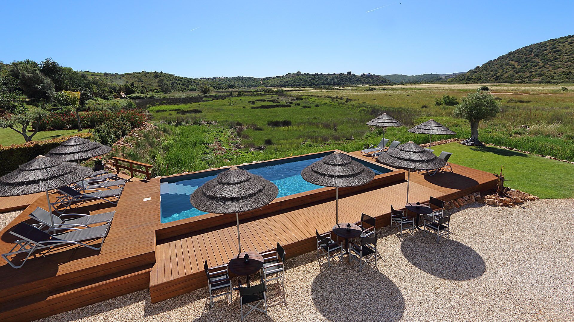 A poolside area with a wooden deck, lounge chairs, and umbrellas.