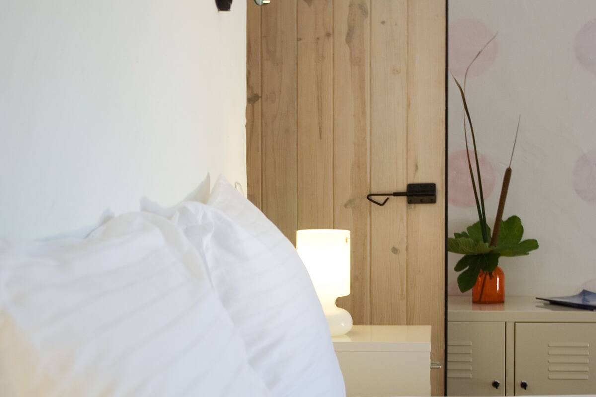 Un dormitorio con un armario de madera, una mesita de noche con una lámpara y una planta en maceta.
