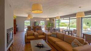A spacious living room with a fireplace, comfortable seating, and large windows offering a view of the outdoors. - Tapada do Gramacho (Lagoa)