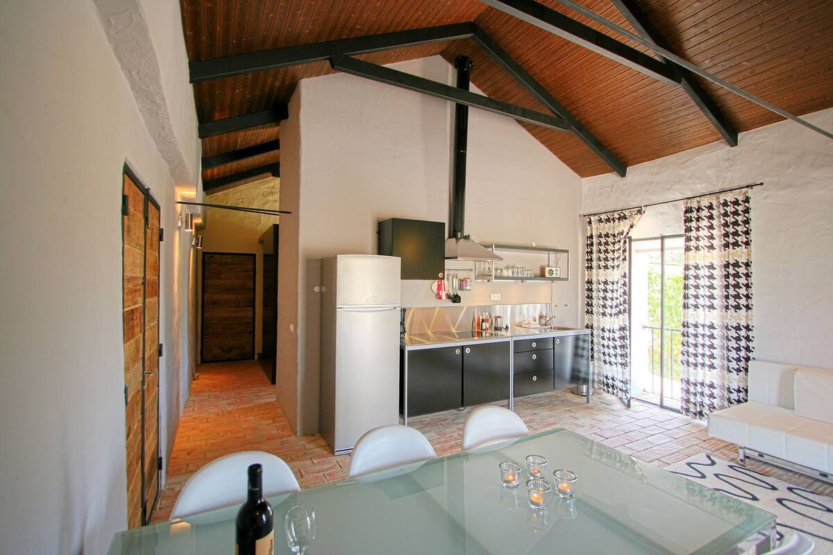 Una cocina moderna con comedor, que incluye una mesa de vidrio, sillas blancas y un sofá blanco.