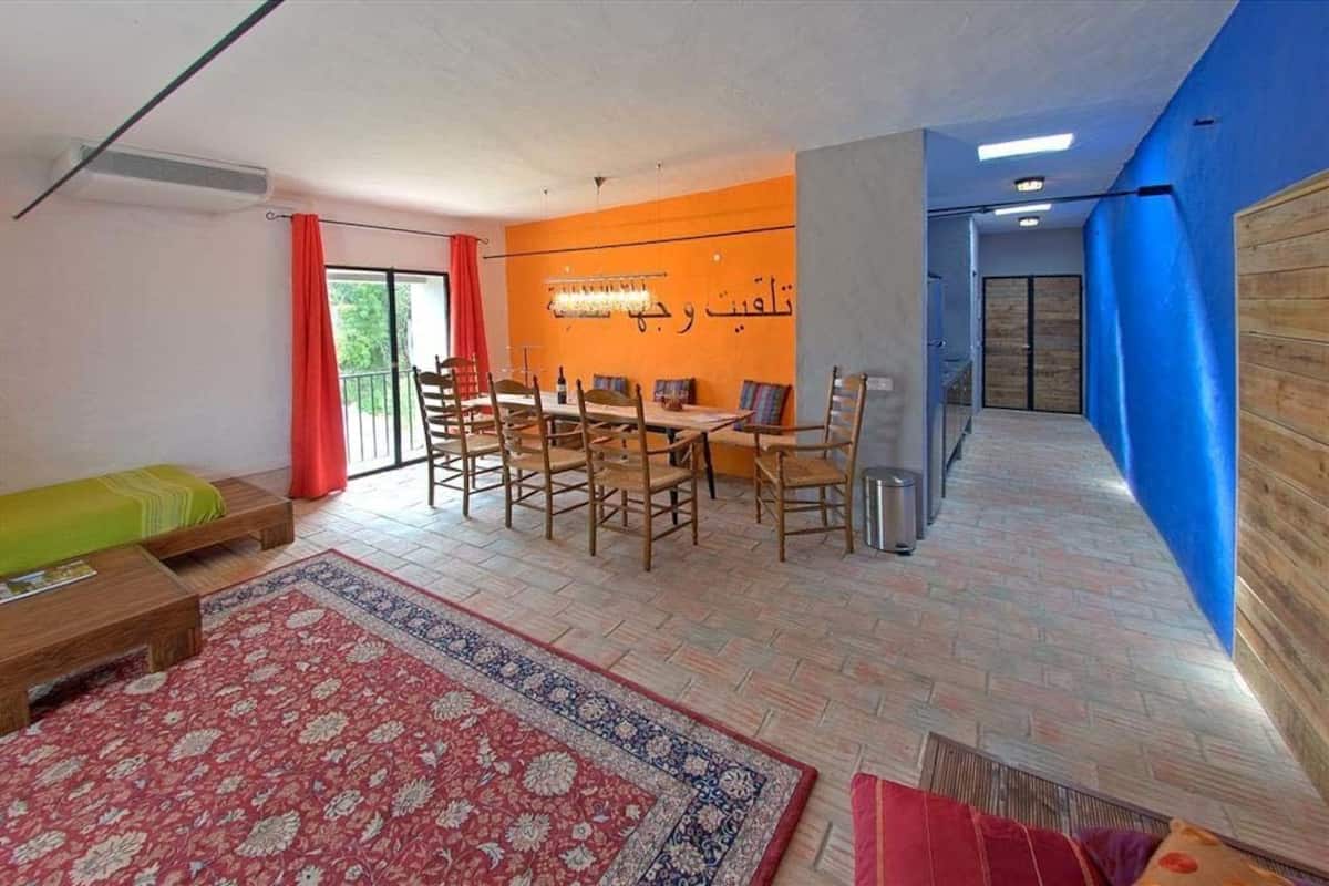 Una sala moderna con comedor, un tapete estampado en rojo y azul, y un banco de madera.
