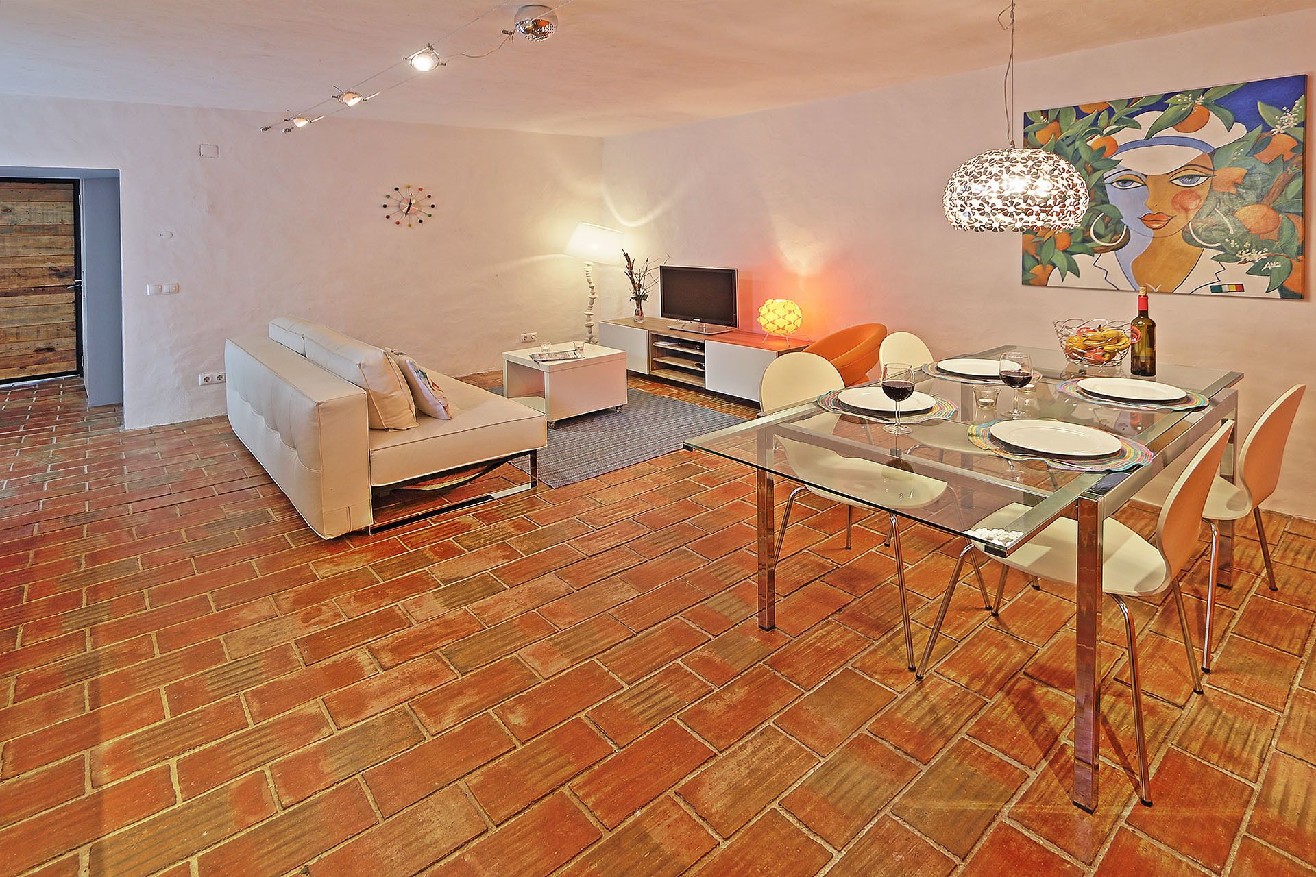 A modern living room with a sofa, TV, and dining area with a glass table and chairs.