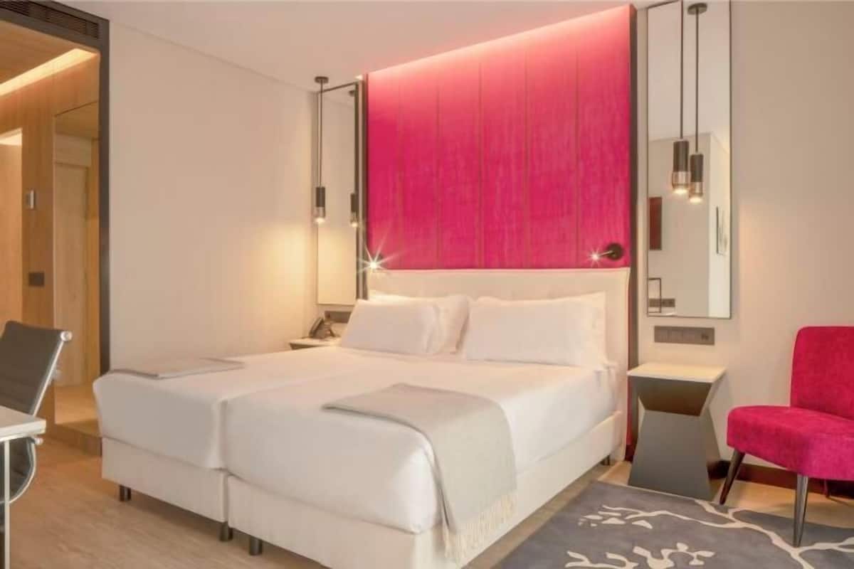 A modern hotel room with a large bed, a desk, a chair, and a mirror.