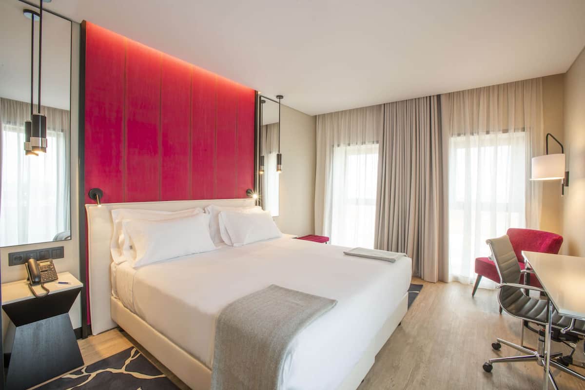 A modern hotel room with a large bed, a desk, a chair, and a telephone.