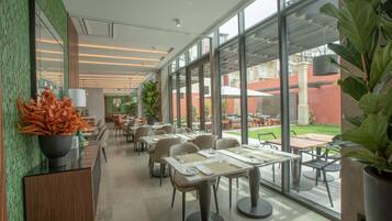 A modern restaurant with large windows, indoor and outdoor seating, and a green wall with a decorative plant.