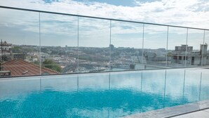 Una piscina infinita en la azotea con vistas despejadas a un paisaje urbano y un puente a lo lejos.