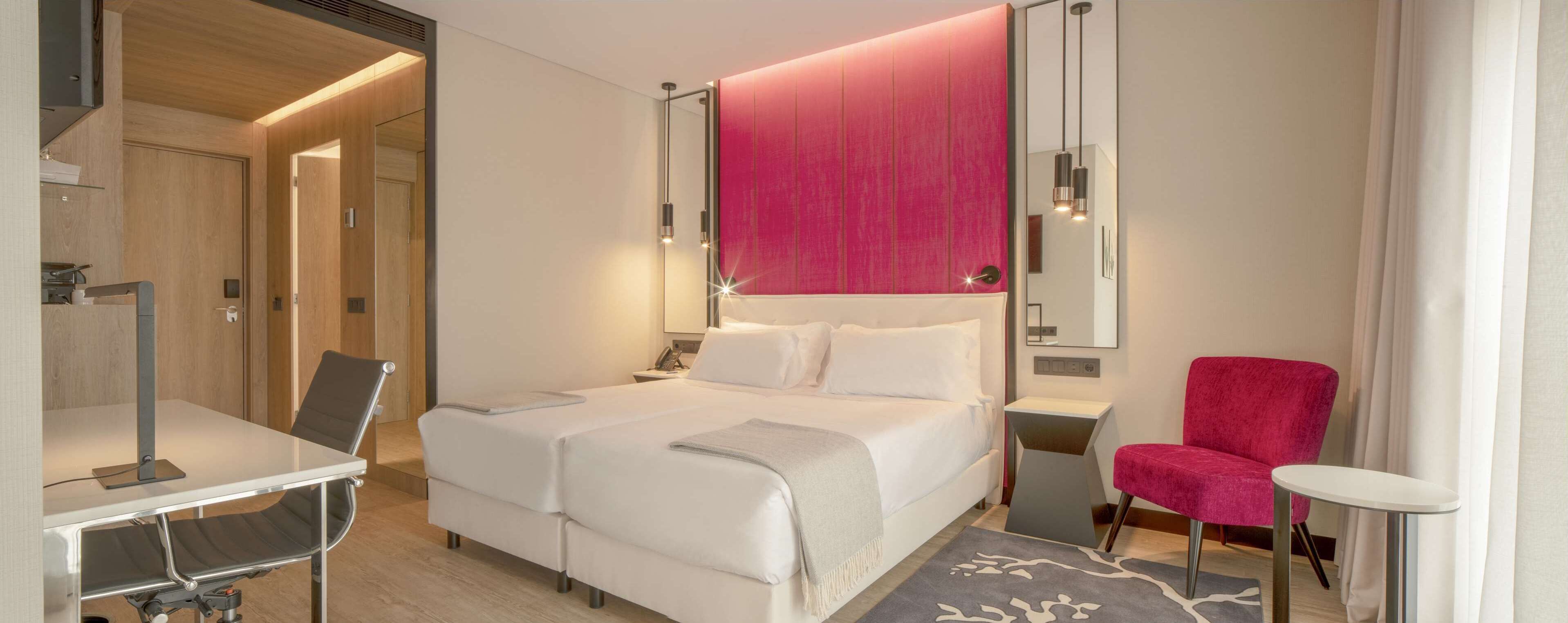 A modern hotel room with a large bed, a desk, and a chair.