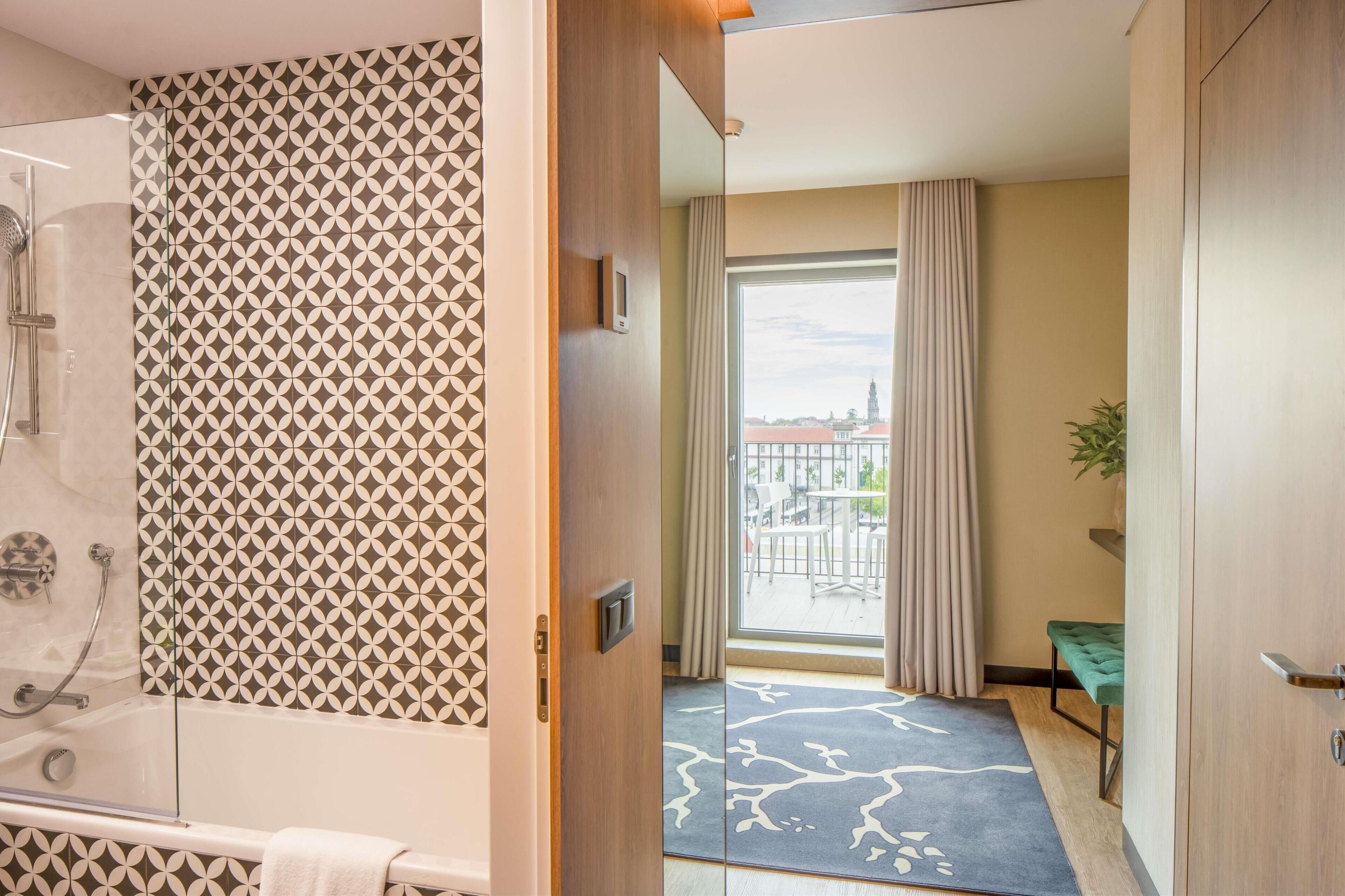 A hotel room with a shower, a patterned wall, a balcony with a view, and a green bench.