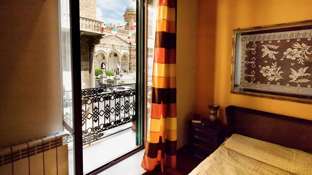 A hotel room with a balcony, a patterned wall hanging, and a view of a historic building. - Entire apartment with Cathedral view, 2 bedrooms and 2 bathrooms, fully equipped (Palermo)
