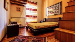 A bedroom with a wooden bed, a bench, a radiator, a window with striped curtains, and a framed picture on the wall. - Entire apartment with Cathedral view, 2 bedrooms and 2 bathrooms, fully equipped (Palermo)