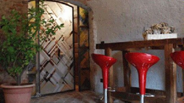 A rustic interior with stone flooring, a brick ceiling, and a wooden table with red bar stools. - B&B San Bernardo (Saluzzo)