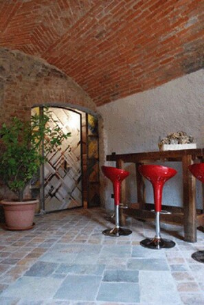 A rustic interior with stone flooring, a brick ceiling, and a wooden table with red bar stools. - B&B San Bernardo (Saluzzo)