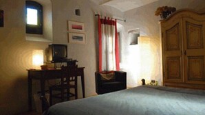 A bedroom with a bed, a desk with a computer, a wardrobe, and a window with curtains. - B&B San Bernardo (Saluzzo)