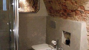 A bathroom with a glass shower enclosure, a white sink, and a bidet. The walls are made of exposed brick, and there is a small window above the sink. - B&B San Bernardo (Saluzzo)