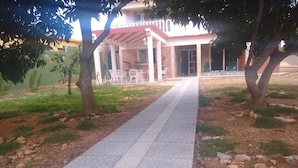 A paved pathway leading to a building with a covered patio area and outdoor seating. - Hostal Los Mangos (Santa Marta)