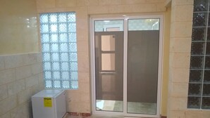 A room with a sliding glass door, a window with a grid pattern, and a small white appliance on the floor. - Hostal Los Mangos (Santa Marta)