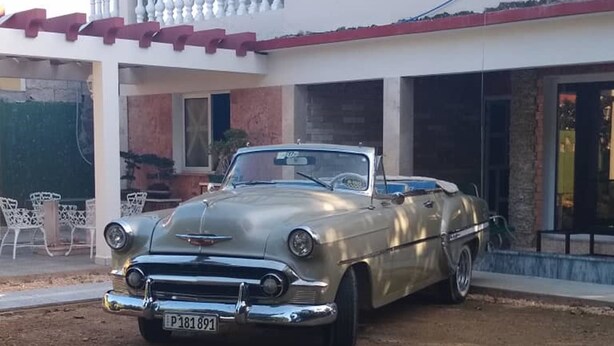 A vintage convertible car parked in front of a two-story house with a balcony. - Hostal Los Mangos (Santa Marta)