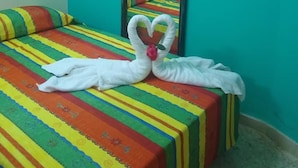 A room with a bed featuring a colorful striped bedspread, a mirror on the wall, and a swan-shaped towel decoration on the bed. - Hostal Los Mangos (Santa Marta)