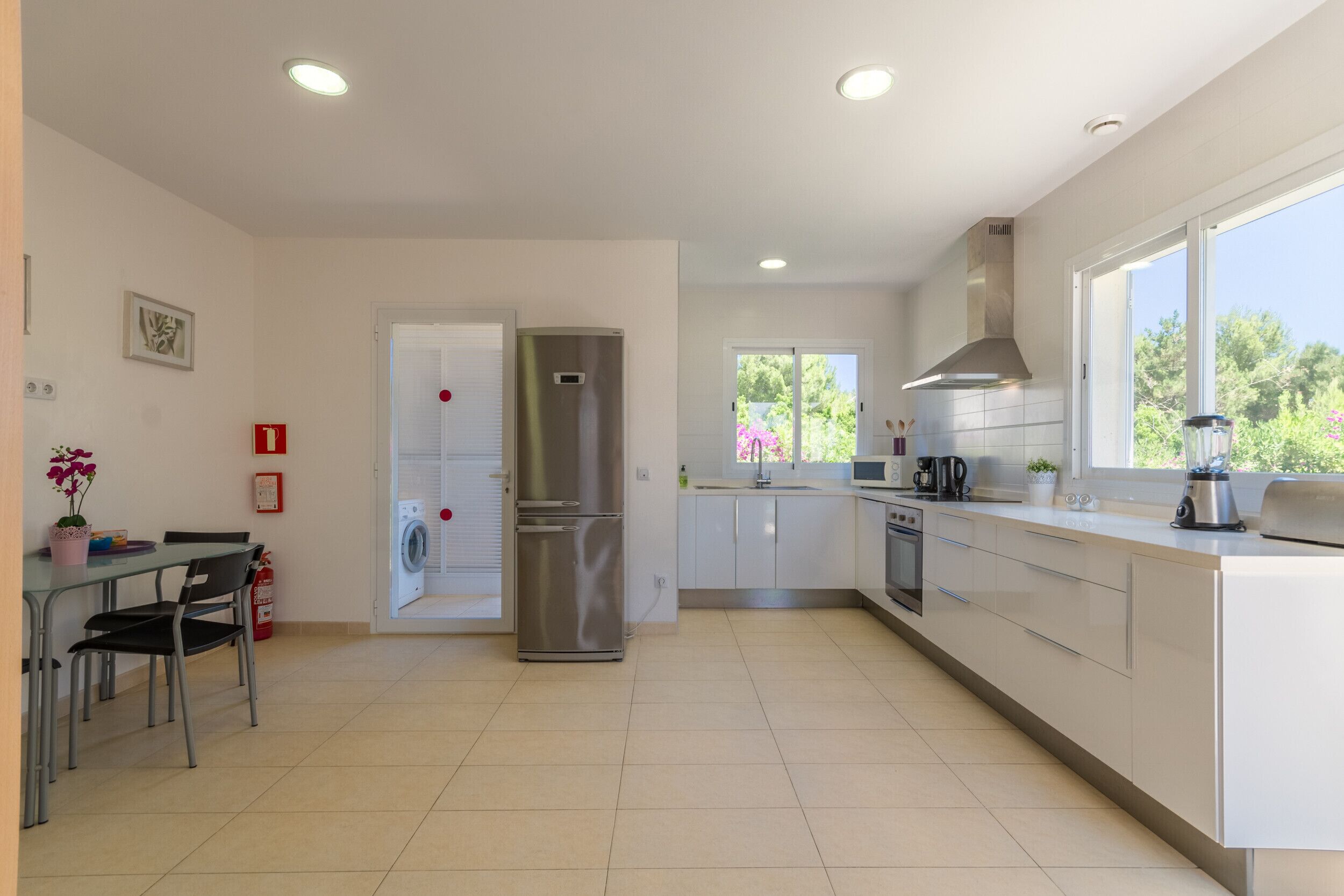 A modern kitchen with a stainless steel refrigerator, a dishwasher, and a sink. There is a window providing natural light and a view of greenery outside.