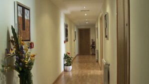 A hallway with wooden flooring, framed pictures on the walls, and potted plants. - Hostal Restaurante La Cepa (Carino)