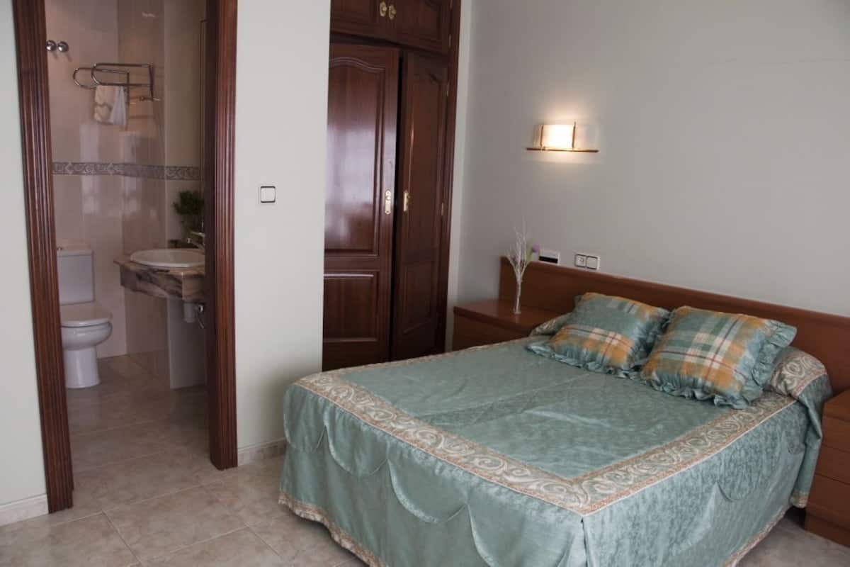 A bedroom with a bed, a nightstand, a wall-mounted lamp, and a wooden door.