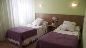 Two single beds with floral bedding and purple headboards in a room with wooden paneling and a nightstand with a plant. - Hostal Restaurante La Cepa (Carino)