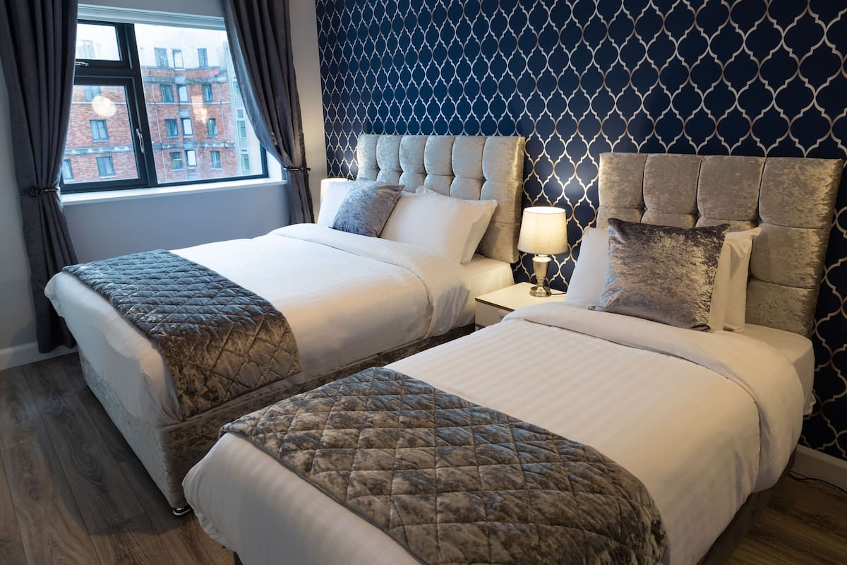 A hotel room with two beds, a nightstand, and a window with curtains.