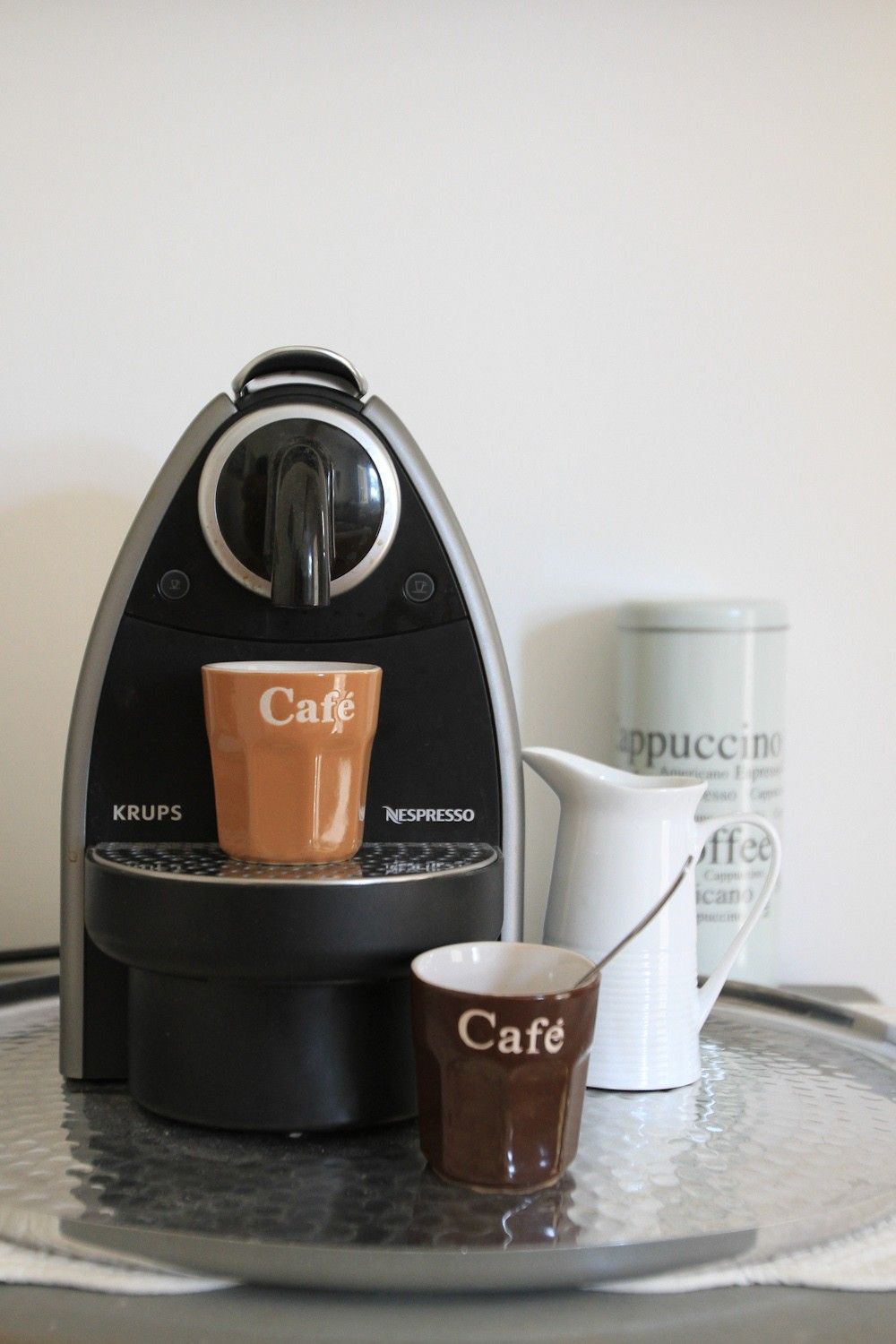 Eine Krups Nespresso Kaffeemaschine mit einer Kaffeetasse und einer weißen Kaffeekanne auf einem Tablett.