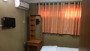 A bedroom with a bed, a wooden nightstand, a mirror, a wall-mounted TV, and an air conditioning unit. - Pent House Appartment (Lagos)