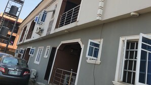 A multi-story residential building with a grey facade, white window frames, and a balcony with a metal railing. - Pent House Appartment (Lagos)