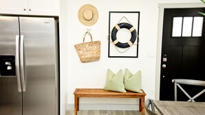 A kitchen with a stainless steel refrigerator, a wooden bench with striped pillows, a straw hat, and a framed life ring on the wall. - ⛱️ O'hana Retreat ⛱️ Great Family Vacay | Spring Savings! (Washington)