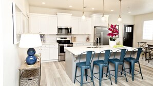 A modern kitchen with white cabinets, stainless steel appliances, a central island with bar stools, and pendant lighting. - ⛱️ O'hana Retreat ⛱️ Great Family Vacay | Spring Savings! (Washington)