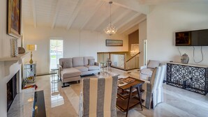 A spacious living room with a fireplace, a sofa, a dining table, and a TV mounted on the wall.