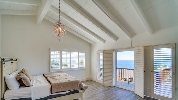 A bedroom with a bed, a chandelier, and a balcony with a view of the ocean.