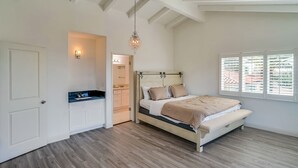 A bedroom with a bed, a chandelier, a window with blinds, and a door.