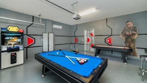 A pool table with a Star Wars-themed arcade machine and a large mural of a character.