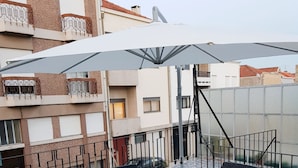 A rooftop patio with wicker furniture, a large umbrella, and a stone-tiled floor. - Enjoy Oporto Flat (Porto)