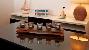 A modern room with a white wall, a wooden shelf with decorative items, a table with candles, and a lamp. - Enjoy Oporto Flat (Porto)