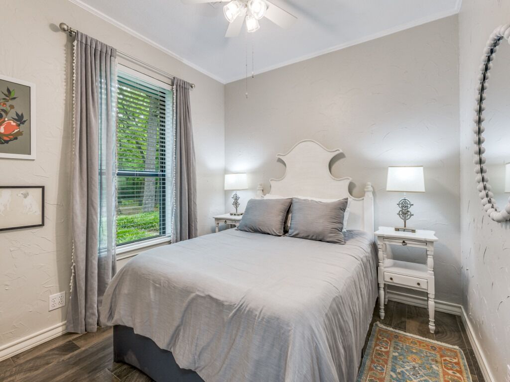 Une chambre à coucher avec un lit, des tables de chevet, un ventilateur de plafond et une fenêtre avec des rideaux.