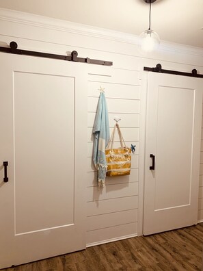Quarto com duas portas brancas, um lustre pendurado e chão de madeira.