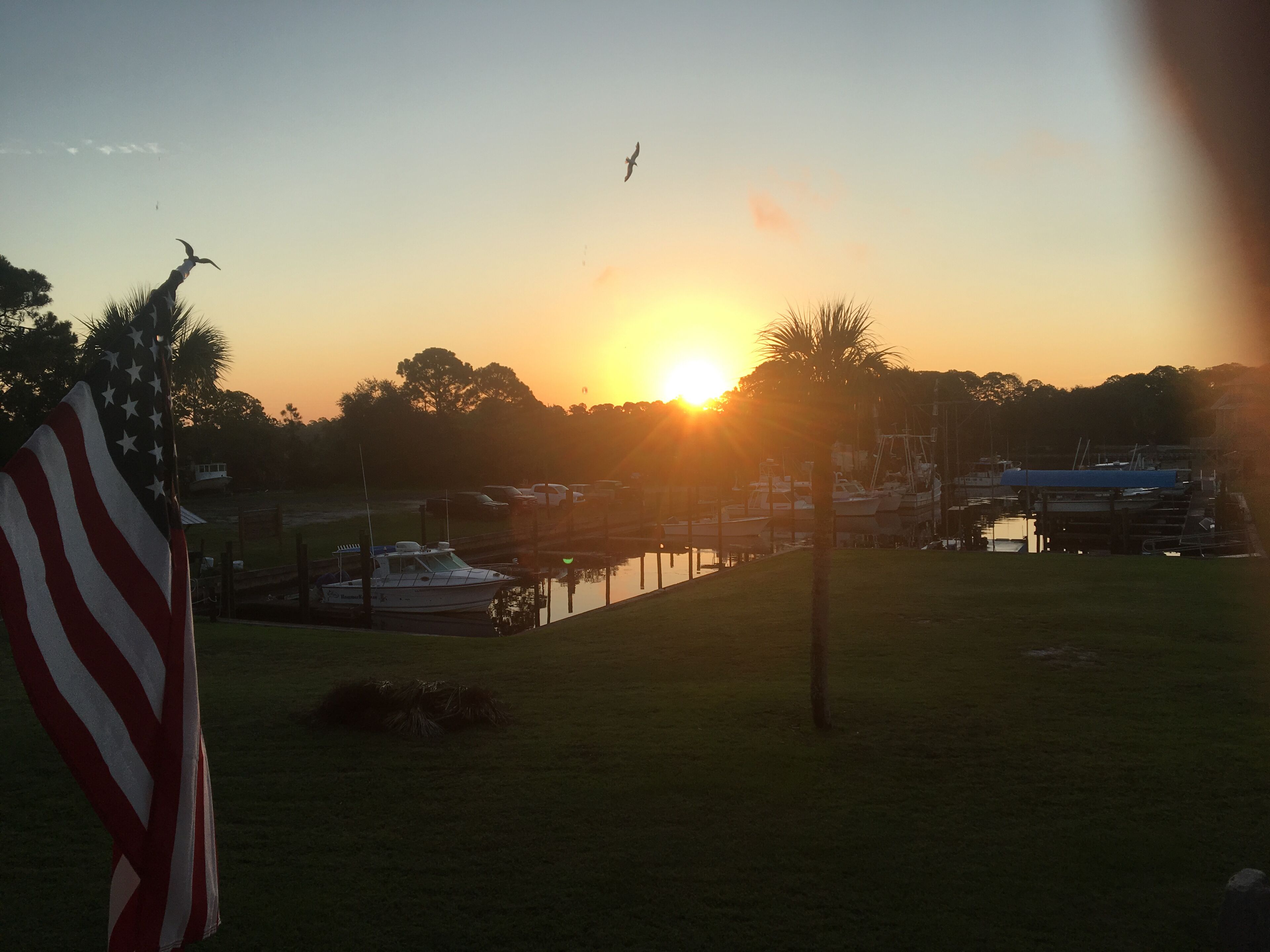 Een jachthaven met aangemeerde boten, een Amerikaanse vlag en een ondergaande zon op de achtergrond.