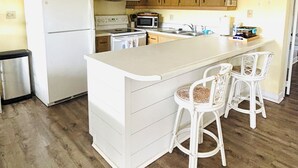 Eine Küche mit Holzschränken, einem weißen Kühlschrank, einer Mikrowelle und einer großen Kochinsel mit Barhocker.